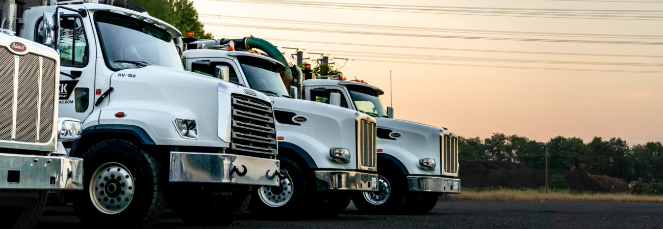 A lineup of white heavy-duty trucks parked in a row on a construction site.
