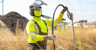 employee wearing hi-visibility gear and ppe working in a remote location in tall grass