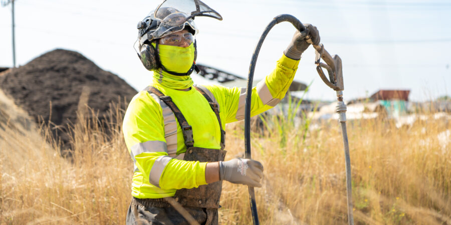 employee wearing hi-visibility gear and ppe working in a remote location in tall grass
