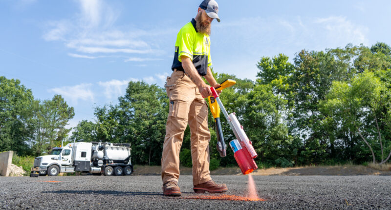 A worker in brown pants and a neon yellow shirt striping lines on a paved area.