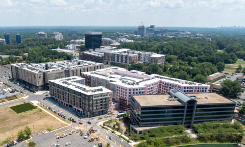 An aerial view of a modern apartment complex under development, with multiple buildings and trees.
