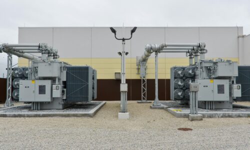 A utility infrastructure site with electrical equipment, pipes, and a gravel surface.