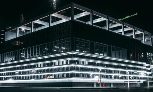 A modern, illuminated building at night with a dark, reflective exterior.