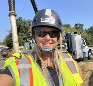 Woman in safety gear standing in front of vacuum truck smiling.